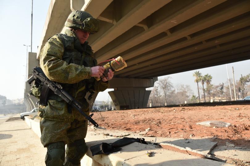 A soldier studies his weaponry as he stands beside a flyover bridge, which was once busy with civilian traffic